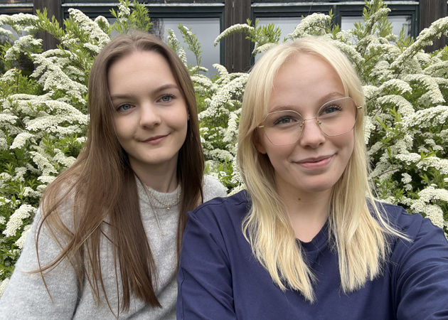 Ellen och Stella fotograferade framför en brudspireabuske i blomning utanfö skolan