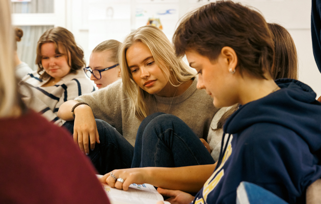 Grupp av studerande tittar i en bok tillsammans.