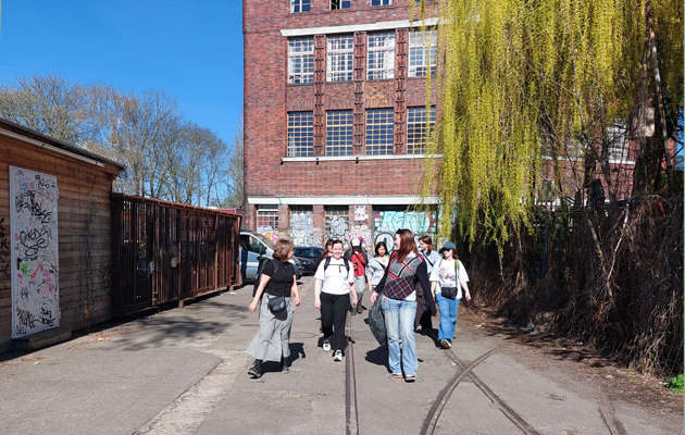 En grupp studerande promenerar i soligt väder med en röd tegelbyggnad i bakgrunden.