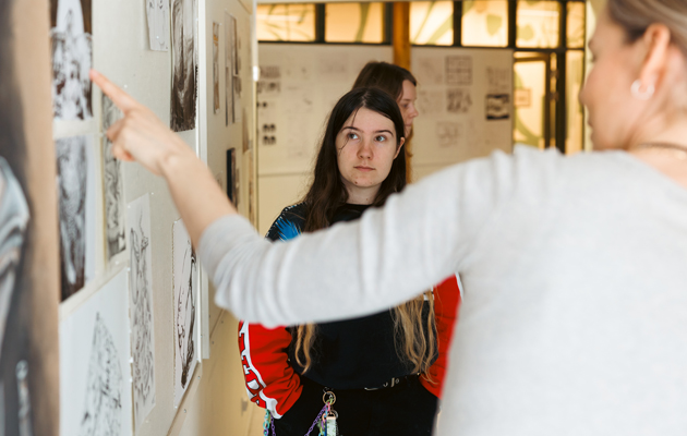 Läraren och studeranden ser på svartvita teckningar som är upphängda på en vägg.