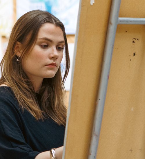 Konststuderande står och målar vid sitt staffli i skolans ateljé.