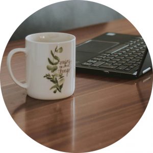 En temugg med texten "Enjoy the little things" står på ett bord. I bakgrunden ser man ett tangentbord.