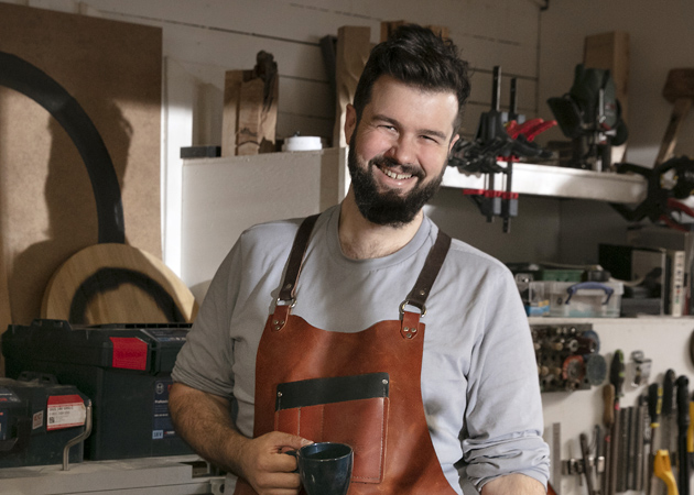 Adam Detre i sin verkstad med en kaffemugg i handen.