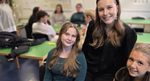 Tre studerande på Natur och medicin linjen poserar leende i klassrummet.