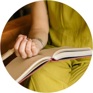 Man ser en skrivbok uppslagen i famnen på en person klädd i gult. Personen har en penna i handen och ser ut att börja skriva. 