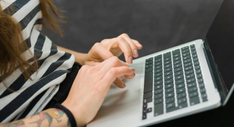 När bild av nänder som skriver på tangentbord. Personen har laptopen i famnen.